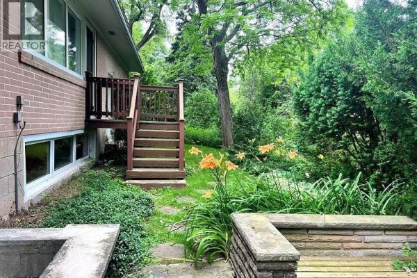 Backyard view of a wooden staircase leading to a deck, surrounded by lush greenery. - 1238 Donlea Crescent Unit# Bsmt, Oakville