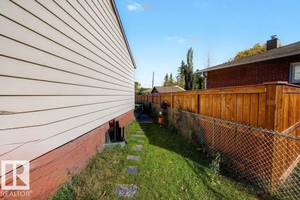 View of the narrow side yard with a stone path, beige siding, and a wooden fence. - 12391 132 St Nw, Edmonton