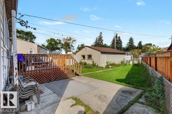 Backyard view with a concrete patio, wooden deck, grass, and a detached garage. - 12391 132 St Nw, Edmonton