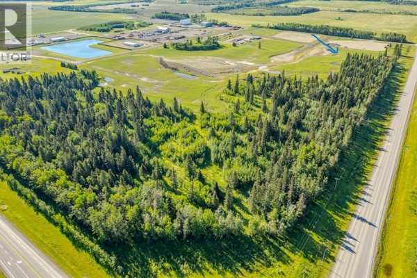 Aerial view of a vast wooded area bordered by a highway and green fields under a blue sky. - 124, 32532 Range Road 42, Rural Mountain View County