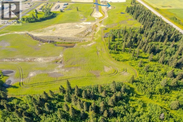 Aerial view of a partially developed lot with tire tracks in the grass and surrounding forest. - 124, 32532 Range Road 42, Rural Mountain View County