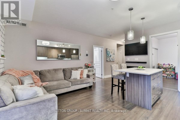 Living room with a grey sectional sofa, kitchen island with bar stools, and wall art. - 124 - 128 Garden Drive, Oakville