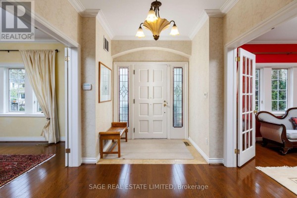 Interior foyer with a white double door, stained glass sidelights, wooden bench, and chandelier. - 124 Blythwood Road, Toronto
