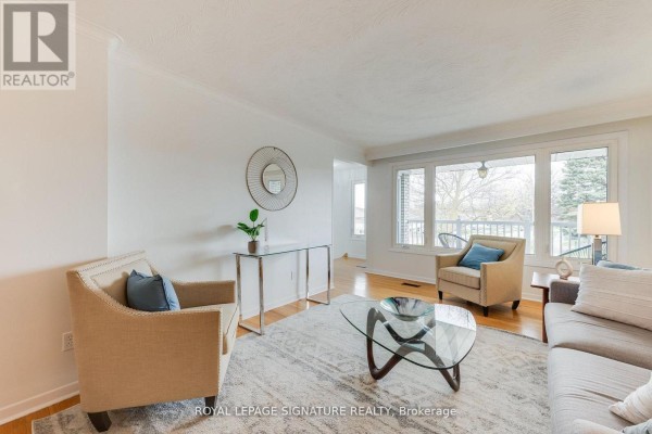 Living room with two beige armchairs, a glass console table, and large windows. - 124 Edmonton Drive, Toronto