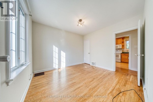 Living room with white sofa, rattan chair, large window, and wooden floor viewed from hallway. - 124 Homewood Avenue, Toronto