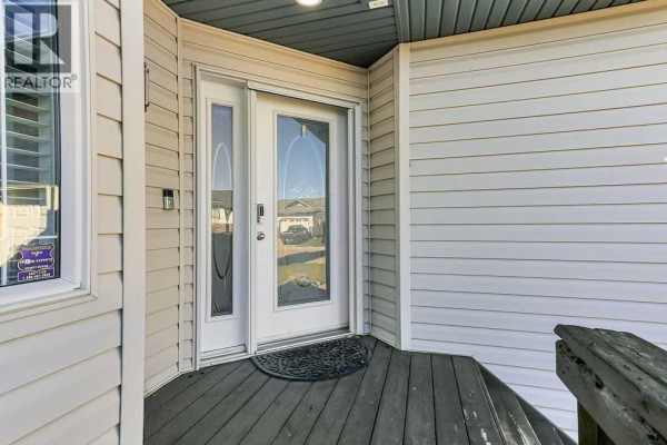 Close-up of the front entrance with a white door and sidelights on a dark wood porch. - 124 Lamont Close, Red Deer