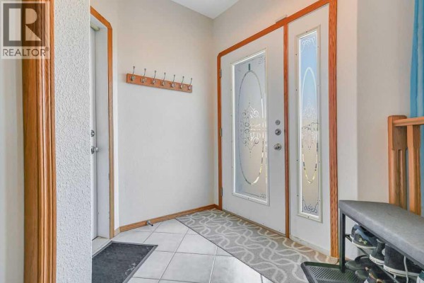 Interior entryway with tiled floor, white door, and coat rack on a beige wall. - 124 Lamont Close, Red Deer