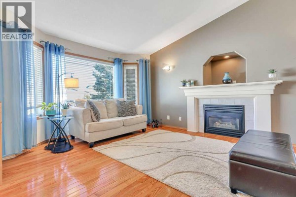 Living room with a fireplace, large bay windows with blue curtains, and hardwood floors. - 124 Lamont Close, Red Deer