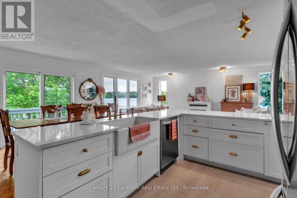 White kitchen island with a farmhouse sink, quartz countertops, and gold hardware overlooks dining area. - 124 Richardson Lane, Prince Edward County