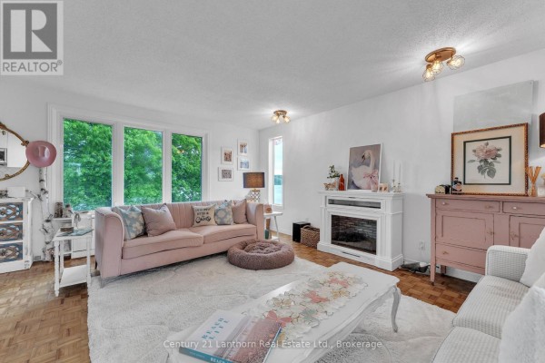 Living room with a pink sofa, two accent chairs, and large windows with a water view. - 124 Richardson Lane, Prince Edward County