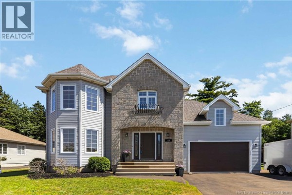 A closer front exterior view of the house with light gray siding, stone accents, and a paved driveway. - 124 Rouse Street, Dieppe