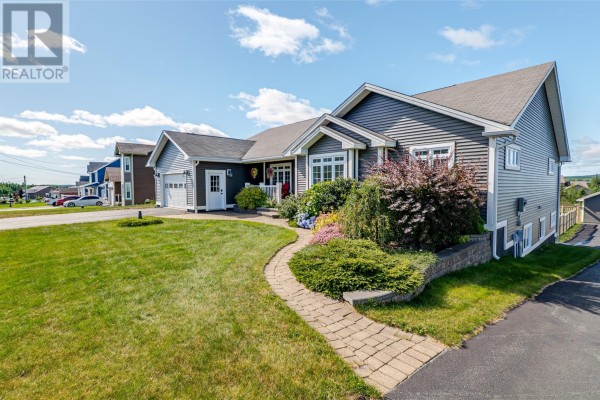 Side view of a bungalow with gray siding, a paved walkway, and lush landscaping. - 124 Sheldon Drive, Bay Bulls