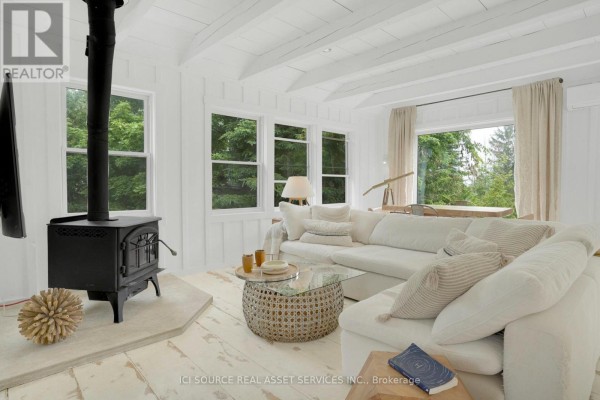 Living room with white sectional sofa, wood stove, and large windows with green trees outside. - 124 Tyrol Avenue, Blue Mountains
