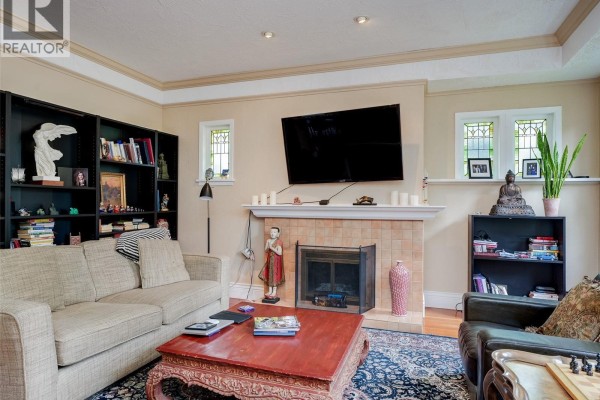 Living room with light beige walls, fireplace, television, and built-in black bookshelves filled with books and decor. - 1240 Victoria Ave, Oak Bay