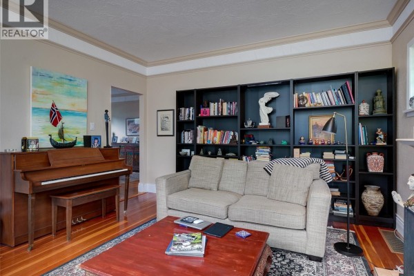 Living room featuring a upright piano, beige sofa, red coffee table, and black bookshelves. - 1240 Victoria Ave, Oak Bay