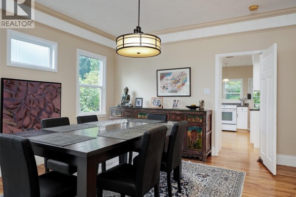 Dining room with dark wood table, black chairs, decorative cabinet, and a view into the kitchen. - 1240 Victoria Ave, Oak Bay