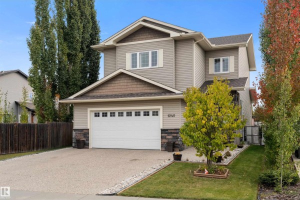 Side view of a residential house featuring beige siding, a garage, and a landscaped front yard. - 1240 Westerra Cr, Stony Plain