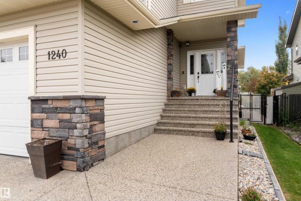 Close-up of the house entrance with stone pillar accents, a white door, and stairs. - 1240 Westerra Cr, Stony Plain