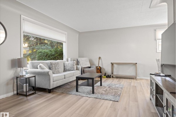 Bright living room with a grey sofa, coffee table, and large window overlooking trees. - 12408 134 St Nw, Edmonton