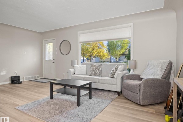 Living room with a sofa, armchair, coffee table, and a window with a view of houses. - 12408 134 St Nw, Edmonton