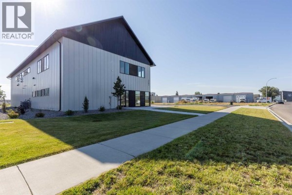 View of a commercial building's side entrance and lawn area, with a concrete walkway extending into the distance. - 1241 29 Street N, Lethbridge
