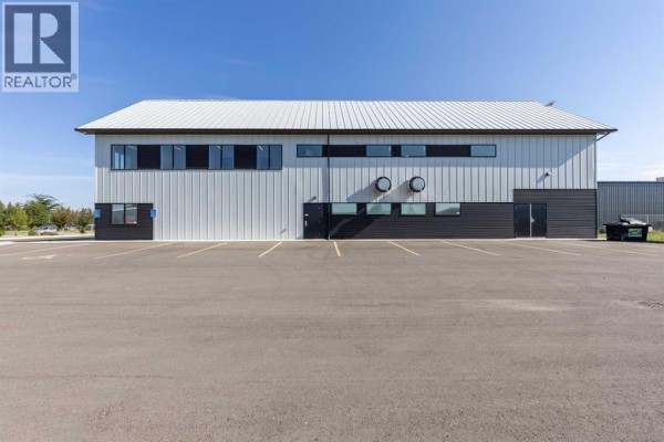 Rear exterior view of a long commercial building with a white metal roof and multiple windows and doors. - 1241 29 Street N, Lethbridge