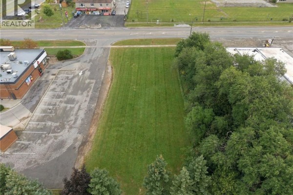 Aerial view showing the grassy lot bordered by a road, trees, and commercial buildings. - 1242 Highway 8, Hamilton