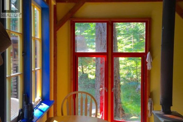 Interior view of the cabin's living area with a red sofa, wood stove, and exposed wooden beams. - 1243/47 Tennyson Rd, Savary Island