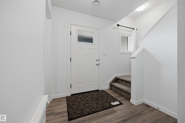 Townhouse entryway with white doors, wood-look flooring, a carpeted staircase, and shoes on the floor. - 1246 Aster Bv Nw, Edmonton