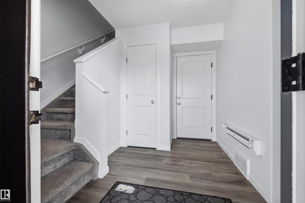 Laundry room with stacked black Samsung washer and dryer, white doors, and clothes on a rack. - 1246 Aster Bv Nw, Edmonton