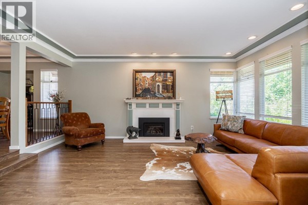 A spacious living room with a tan leather sectional sofa, a decorative fireplace, and a patterned armchair on wood-look flooring. - 12461 205 Street, Maple Ridge
