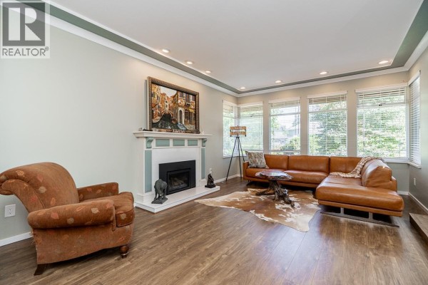 A living room featuring a fireplace with a white mantel, a large tan sectional sofa, and large windows overlooking greenery. - 12461 205 Street, Maple Ridge
