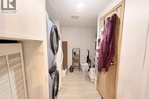 Laundry room with stacked washer and dryer, refrigerator, and storage shelves against a white wall. - 125 1 Avenue, Leslieville