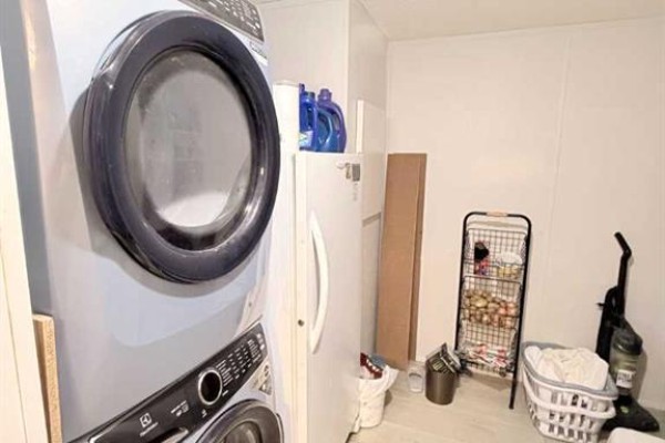Close-up of stacked washer and dryer, refrigerator, and laundry baskets in a utility room. - 125 1 Avenue, Leslieville