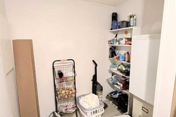 Rear view of a laundry room showing shelves stocked with various items, a vacuum cleaner, and a cart of produce. - 125 1 Avenue, Leslieville
