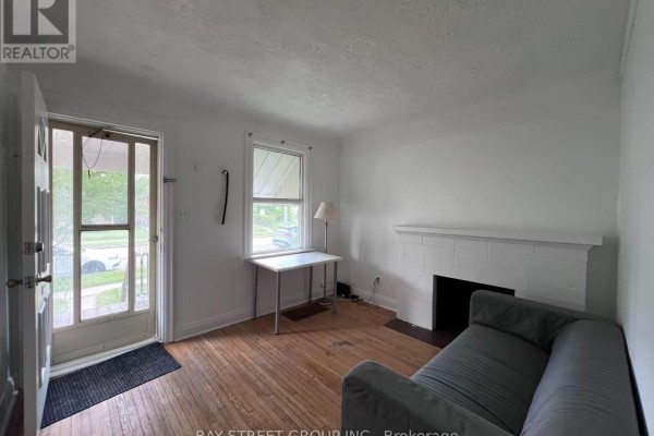 Living room with a grey sofa, white fireplace, hardwood floors, and kitchen view. - 125 Broadway Avenue, Hamilton