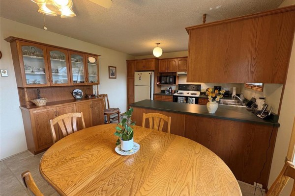 Oak dining table and chairs in front of a kitchen island with dark countertops. - 125 Dunfield Avenue, Dauphin