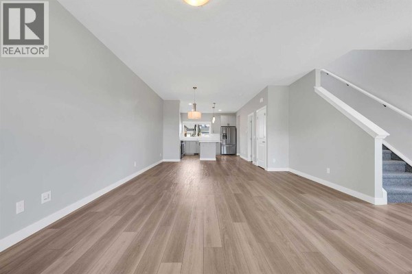 Open concept main floor with living area, kitchen with island, and staircase with grey carpeted steps. - 125 Edith Gate Nw, Calgary