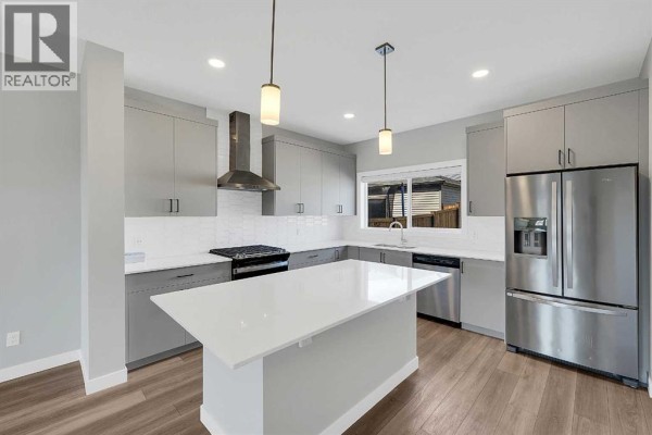 Contemporary kitchen featuring light grey cabinets, quartz countertops, stainless steel appliances, and a central island. - 125 Edith Gate Nw, Calgary