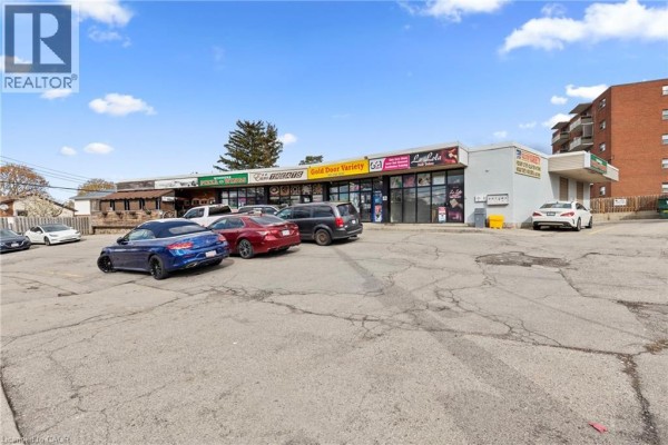 Exterior view of a commercial strip mall from the parking lot showing store fronts and surrounding vehicles. - 125 Gailmont Drive, Hamilton