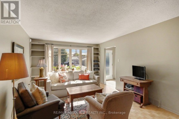 Living room with a sofa, chairs, built-in bookshelves, and a large bay window overlooking the yard. - 125 Juniper Street E, Ottawa