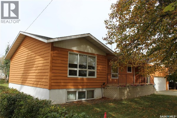 Kitchen counter area with a double sink, wooden cabinets, and a window view. - 125 Mainprize Street, Midale