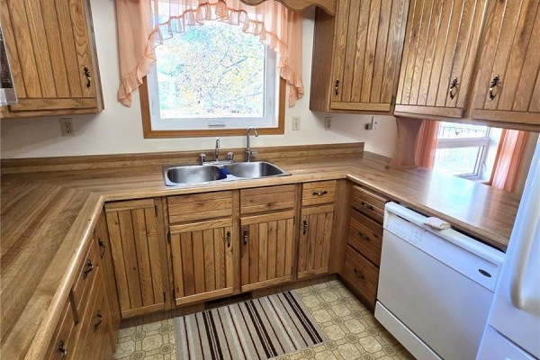 Kitchen showing a white refrigerator, wooden cabinets, dishwasher, and hallway view. - 125 Mainprize Street, Midale