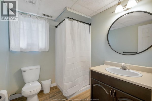 Bathroom with toilet, vanity, sink, round mirror, and shower curtain - 125 Queen Street South Tilbury