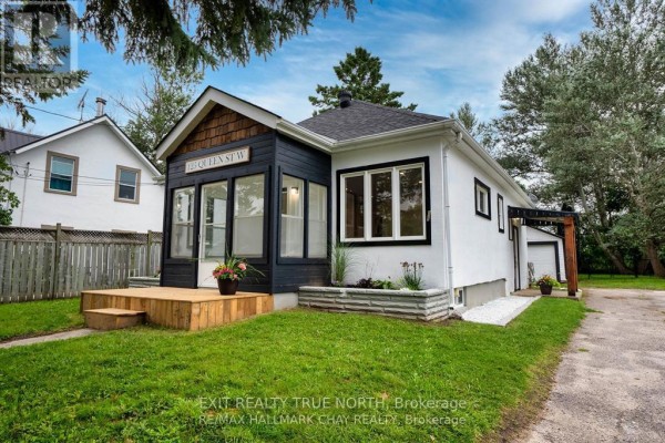 Side view of a white bungalow featuring a dark wood enclosed porch, new windows, and a wooden pergola over a side entrance. - 125 Queen Street W, Springwater