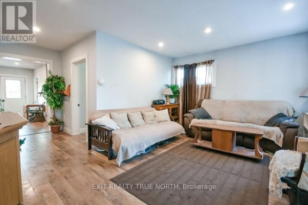 Living room with light blue walls, wood-look laminate flooring, two sofas, a coffee table, and a doorway leading to another room. - 125 Queen Street W, Springwater