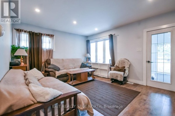 Living room showing two sofas, a brown rug, large windows with brown curtains, and a glass-paneled door leading outside. - 125 Queen Street W, Springwater