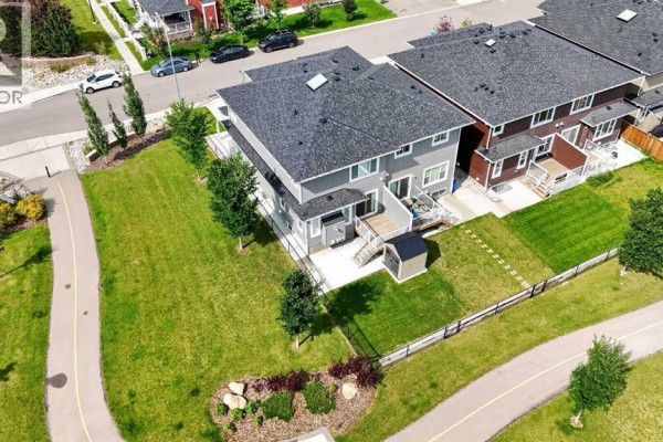 Rear aerial view of a duplex with a deck, fenced yard, shed, and walking path. - 125 Redstone Common Ne, Calgary