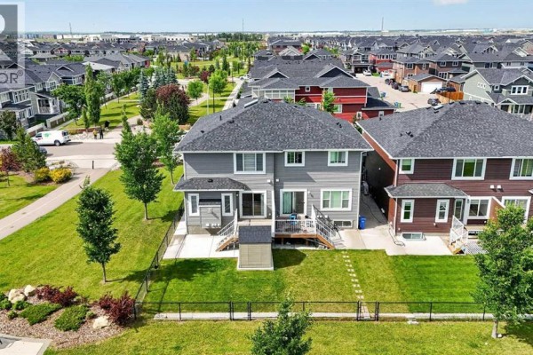 Aerial view of the rear of duplexes showing backyards, fenced areas, and a neighborhood street. - 125 Redstone Common Ne, Calgary