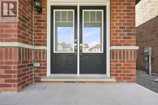 Exterior front view of a two-story suburban house on a sunny day with a stone and vinyl facade. - 125 Tumblewood Place, Welland